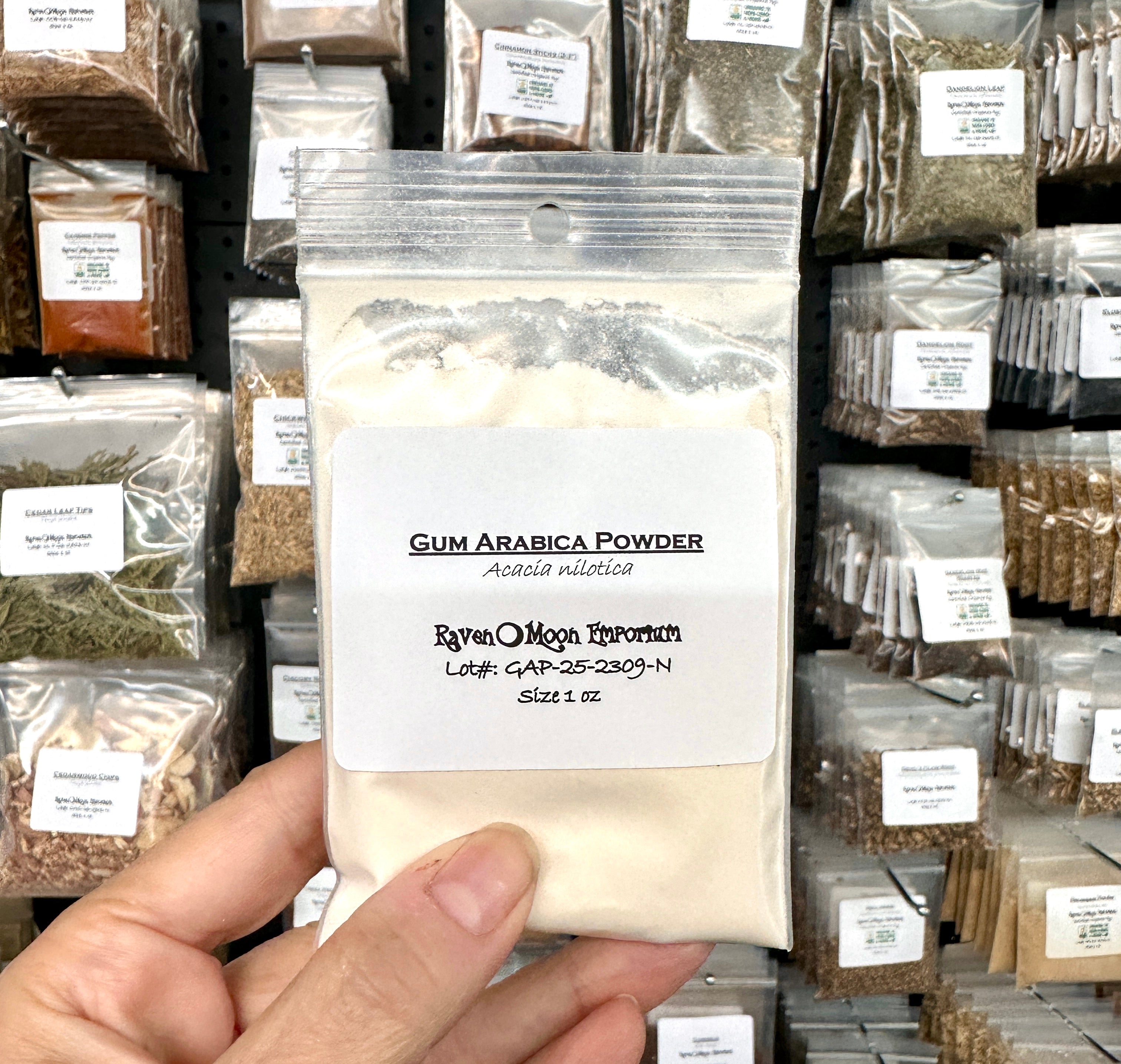 Hand holding a package of Gum Arabica Powder with a background of similar packages.